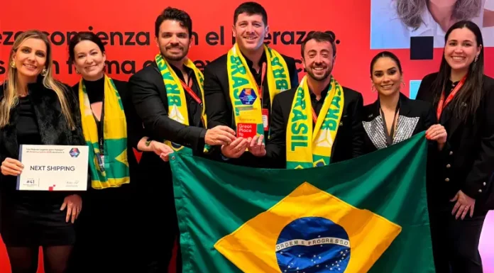 Representantes da Next Shipping posam segurando a bandeira do Brasil e exibindo medalhas e o certificado recebidos durante a cerimônia de premiação do ranking Great Place To Work 2025, em reconhecimento à excelência na gestão de pessoas.