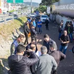 Prefeitura de São José inicia revitalização de áreas críticas para impedir ocupações irregulares Na foto, várias pessoas estão vistoriando uma área vulnerável em um beco estreito, localizado ao lado da Via Expressa, em São José. O grupo caminha e observa o local, que tem vegetação rasteira,e algumas estruturas precárias. O ambiente transmite sensação de abandono e vulnerabilidade.