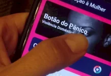 Mão segurando um celular enquanto aciona o Botão do Pânico no aplicativo PMSC Cidadão, usado para prevenir violência contra a mulher em Santa Catarina.