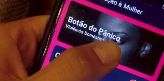 Mão segurando um celular enquanto aciona o Botão do Pânico no aplicativo PMSC Cidadão, usado para prevenir violência contra a mulher em Santa Catarina.