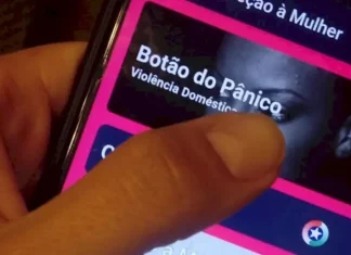 Mão segurando um celular enquanto aciona o Botão do Pânico no aplicativo PMSC Cidadão, usado para prevenir violência contra a mulher em Santa Catarina.