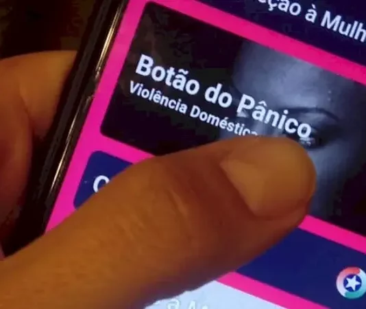 Mão segurando um celular enquanto aciona o Botão do Pânico no aplicativo PMSC Cidadão, usado para prevenir violência contra a mulher em Santa Catarina.