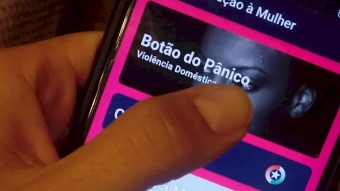 Mão segurando um celular enquanto aciona o Botão do Pânico no aplicativo PMSC Cidadão, usado para prevenir violência contra a mulher em Santa Catarina.