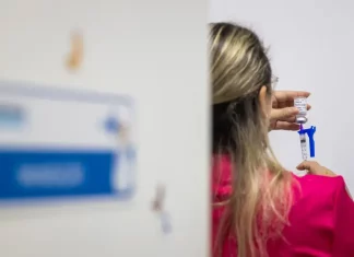 Imagem de enfermeira preparando uma seringa com a vacina contra a Influenza, em um ambiente de saúde, durante a vacinação dos grupos prioritários.
