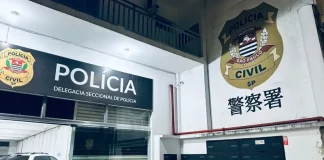 Fachada interna de uma delegacia de polícia. A imagem mostra uma porta de vidro aberta. Acima da porta, está a logo da Polícia Civil e a inscrição "Delegacia Seccional de Polícia". Do lado de fora, no pátio, há um carro branco estacionado.