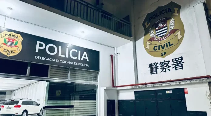 Fachada interna de uma delegacia de polícia. A imagem mostra uma porta de vidro aberta. Acima da porta, está a logo da Polícia Civil e a inscrição "Delegacia Seccional de Polícia". Do lado de fora, no pátio, há um carro branco estacionado.