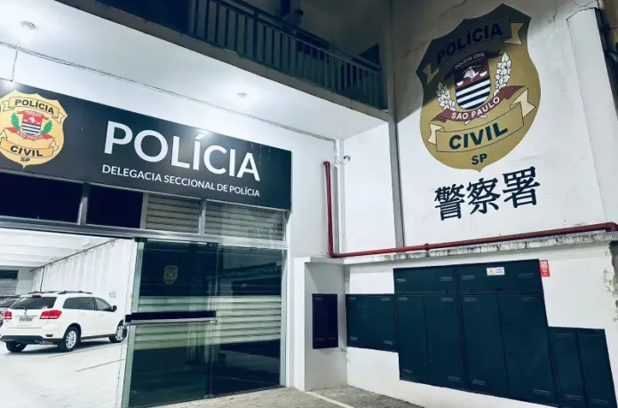 Fachada interna de uma delegacia de polícia. A imagem mostra uma porta de vidro aberta. Acima da porta, está a logo da Polícia Civil e a inscrição 