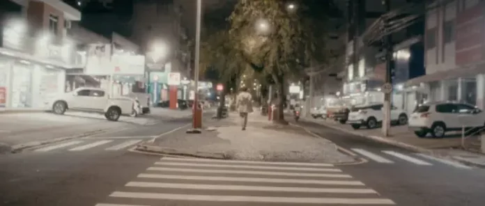 Pessoa caminha à noite pelo calçadão iluminado do centro de São José, SC, cenário do filme Peça para Solidão Solo.