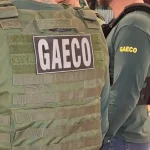 Foto mostra dois policiais do Gaeco de costas, ambos usando coletes à prova de balas.