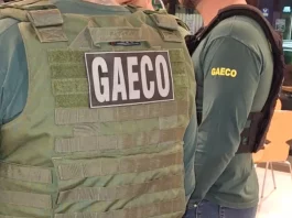 Foto mostra dois policiais do Gaeco de costas, ambos usando coletes à prova de balas.
