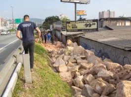 Homem de camiseta azul caminhando na marginal da Via Expressa, ao lado de pedras pontiagudas colocadas pela prefeitura para evitar ocupações irregulares.