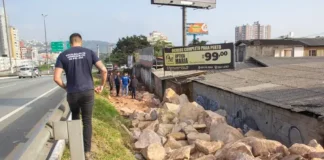 Homem de camiseta azul caminhando na marginal da Via Expressa, ao lado de pedras pontiagudas colocadas pela prefeitura para evitar ocupações irregulares.