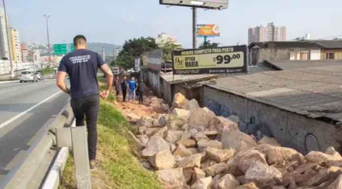 Homem de camiseta azul caminhando na marginal da Via Expressa, ao lado de pedras pontiagudas colocadas pela prefeitura para evitar ocupações irregulares.