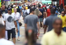Multidão de pessoas caminhando em área central de uma grande cidade, representando o aumento da população urbana e o crescimento populacional nas regiões metropolitanas.