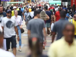 Multidão de pessoas caminhando em área central de uma grande cidade, representando o aumento da população urbana e o crescimento populacional nas regiões metropolitanas.