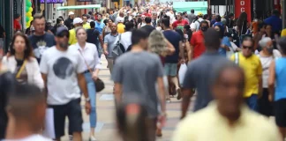 Multidão de pessoas caminhando em área central de uma grande cidade, representando o aumento da população urbana e o crescimento populacional nas regiões metropolitanas.