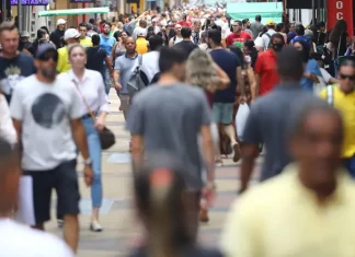 Multidão de pessoas caminhando em área central de uma grande cidade, representando o aumento da população urbana e o crescimento populacional nas regiões metropolitanas.