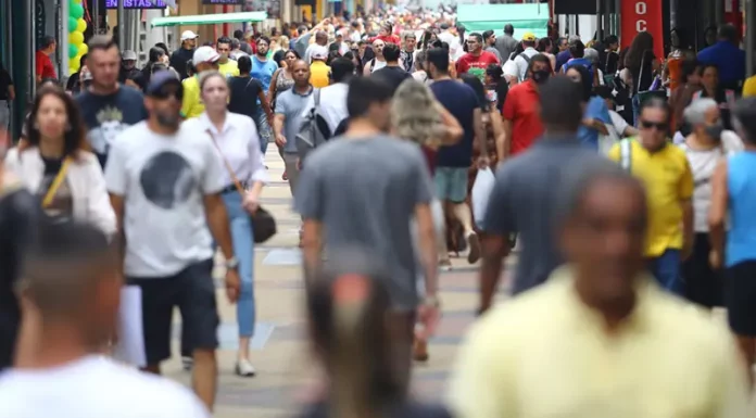 Multidão de pessoas caminhando em área central de uma grande cidade, representando o aumento da população urbana e o crescimento populacional nas regiões metropolitanas.
