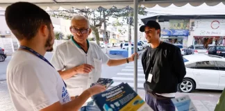 Homem de camiseta branca segurando um panfelto do Trato Pelo Araujo, conversanbdo com um senhor de camisa branca, usando óculos e com um homem de camisa preta e boné