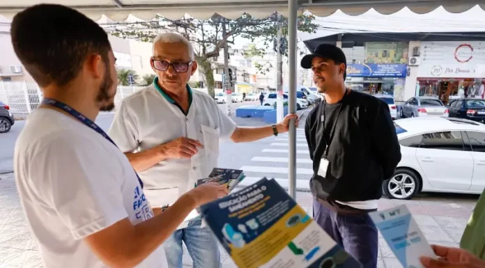 Homem de camiseta branca segurando um panfelto do Trato Pelo Araujo, conversanbdo com um senhor de camisa branca, usando óculos e com um homem de camisa preta e boné