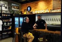 Homem aprecia cerveja artesanal no balcão do bar da Unika, em Coqueiros, enquanto atendente entrega o copo.