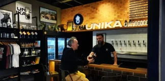 Homem aprecia cerveja artesanal no balcão do bar da Unika, em Coqueiros, enquanto atendente entrega o copo.