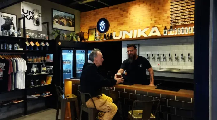 Homem aprecia cerveja artesanal no balcão do bar da Unika, em Coqueiros, enquanto atendente entrega o copo.