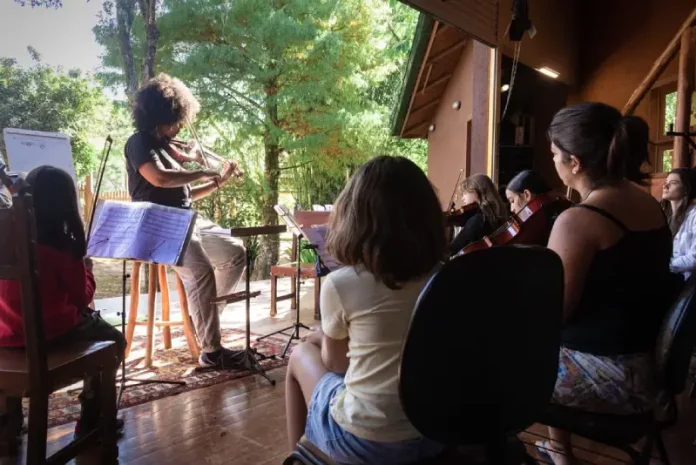 Crianças aprendendo a tocar violino durante oficina do Festival Multicultural na Guarda do Embaú.
