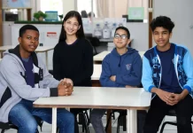 Estudantes migrantes — três meninos e uma menina — sentados juntos em uma mesa de sala de aula