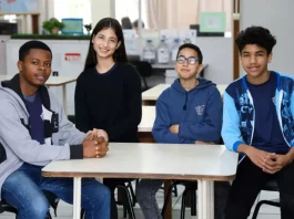 Estudantes migrantes — três meninos e uma menina — sentados juntos em uma mesa de sala de aula