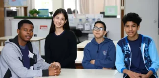 Estudantes migrantes — três meninos e uma menina — sentados juntos em uma mesa de sala de aula
