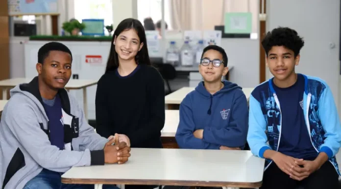 Estudantes migrantes — três meninos e uma menina — sentados juntos em uma mesa de sala de aula