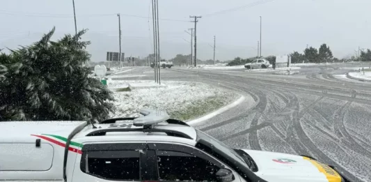 Viatura da Polícia Militar parada em um trevo na entrada de uma cidade da Serra Catarinense, com neve cobrindo o asfalto durante a Operação Estação Inverno.