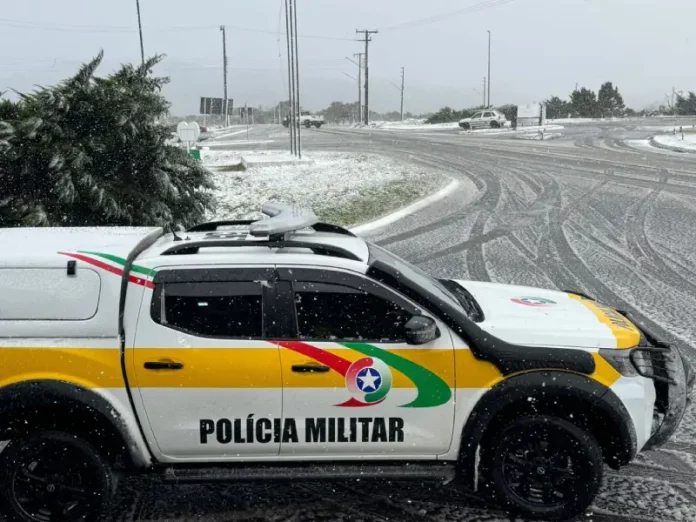 Viatura da Polícia Militar parada em um trevo na entrada de uma cidade da Serra Catarinense, com neve cobrindo o asfalto durante a Operação Estação Inverno.