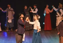 Integrantes da categoria adulta de danças tradicionais do Grupo Querência Açoriana se apresentam no palco durante a Fegasc, vestindo trajes típicos e executando coreografia gaúcha.