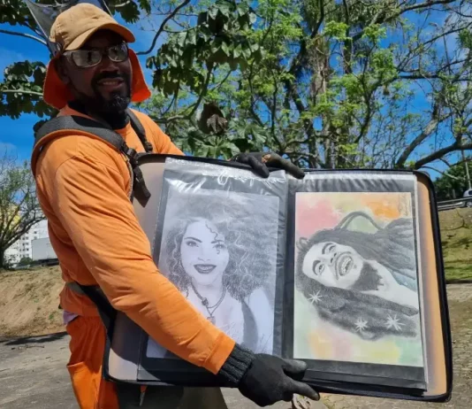 Luciano do Carmo de Paula, roçador de São José, com uniforme de trabalho, segurando uma pasta com seus desenhos artísticos.