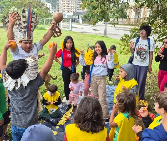 Estudantes e comunidade indígena compartilham um piquenique na agrofloresta, fortalecendo a troca de saberes tradicionais e práticas sustentáveis.