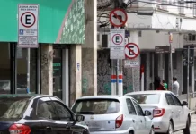 Carros estacionados nas vagas da Zona Azul em Florianópolis, com placas de sinalização ao fundo.
