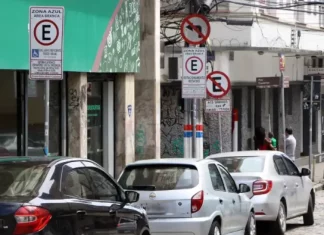 Carros estacionados nas vagas da Zona Azul em Florianópolis, com placas de sinalização ao fundo.