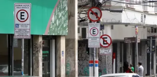 Carros estacionados nas vagas da Zona Azul em Florianópolis, com placas de sinalização ao fundo.