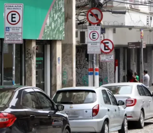 Carros estacionados nas vagas da Zona Azul em Florianópolis, com placas de sinalização ao fundo.