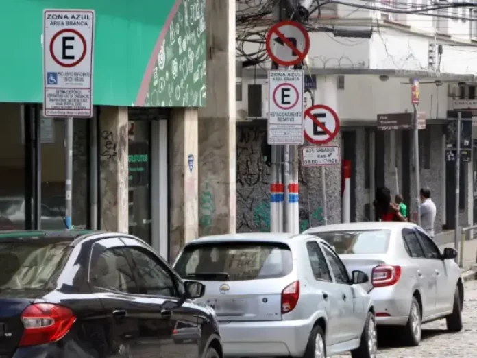 Carros estacionados nas vagas da Zona Azul em Florianópolis, com placas de sinalização ao fundo.