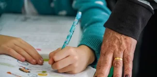 Pessoa adulta acompanha criança durante atividade de escrita, simbolizando ações de combate ao analfabetismo e incentivo à alfabetização na educação básica.