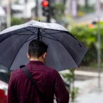 Primavera será marcada por chuvas mais frequentes em Santa Catarina Homem caminhando na chuva com guarda-chuva, representando o início da primavera com aumento das chuvas em Santa Catarina