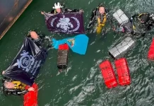 Mergulhadores táticos da Polícia Federal recolhendo pacotes de cocaína escondidos no casco submerso de navio no porto de Imbituba.