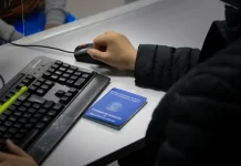 Braço de um homem usando o mouse ao lado de um teclado, com uma carteira de trabalho sobre a mesa, ilustrando o registro e controle de empregos formais em Santa Catarina.