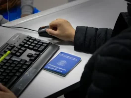 Santa Catarina acumula 83,8 mil novas vagas de empregos formais em 2025 Braço de um homem usando o mouse ao lado de um teclado, com uma carteira de trabalho sobre a mesa, ilustrando o registro e controle de empregos formais em Santa Catarina.