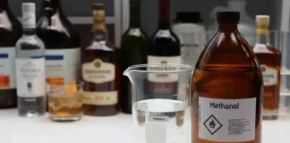 Mesa exibe diversas garrafas de bebidas alcoólicas ao lado de um frasco de metanol, ilustrando o alerta do Procon/SC sobre riscos de adulteração e intoxicação por metanol.
