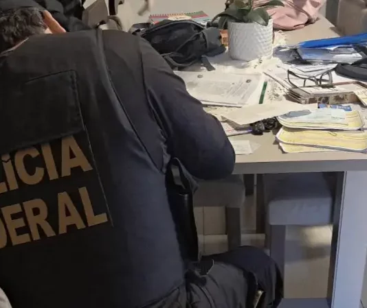 Polícia Federal investiga fraude eletrônica contra a Caixa Econômica Federal em Santa Catarina Agente da Polícia Federal analisando documentos durante cumprimento de mandado de busca na Operação Alea, em Santa Catarina.
