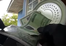 Mãos de policial federal segurando documentos apreendidos durante operação que investiga fraude bancária.